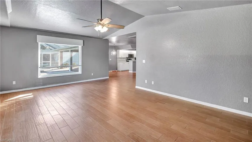 Empty room featuring a textured wall, vaulted ceiling, a ceiling fan, a textured ceiling, and light wood-style flooring