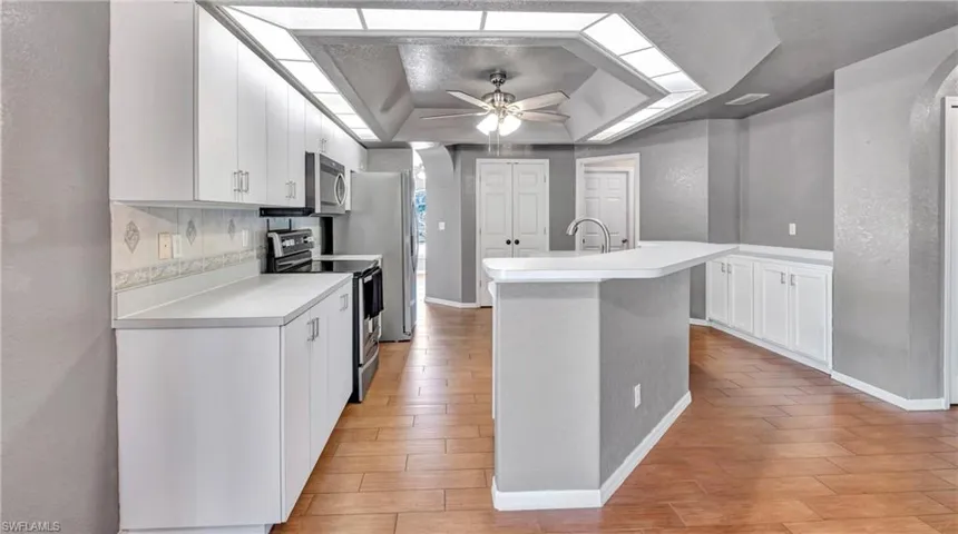 Kitchen featuring a textured wall, white cabinetry, appliances with stainless steel finishes, light countertops, and a center island with sink