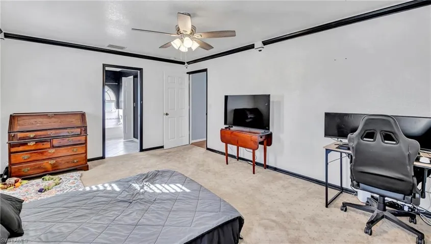 Bedroom with light colored carpet, crown molding, ceiling fan, an office area, and ensuite bath