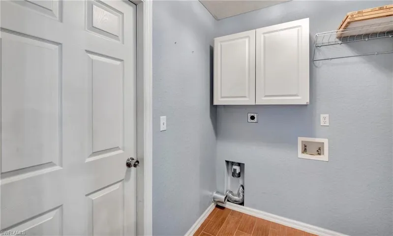 Laundry area with a textured wall, electric dryer hookup, cabinet space, wood finish floors, and washer hookup