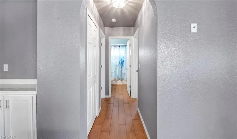 Hallway with a textured wall, light wood-style flooring, and a textured ceiling