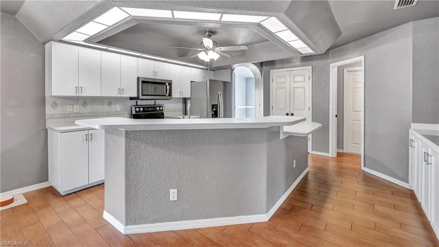 Kitchen featuring light countertops, white cabinets, a textured wall, light wood-style floors, and stainless steel appliances