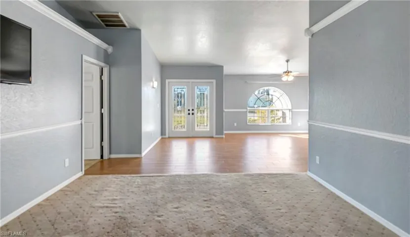 Unfurnished living room featuring crown molding, french doors, a textured wall, ceiling fan, and wood finished floors