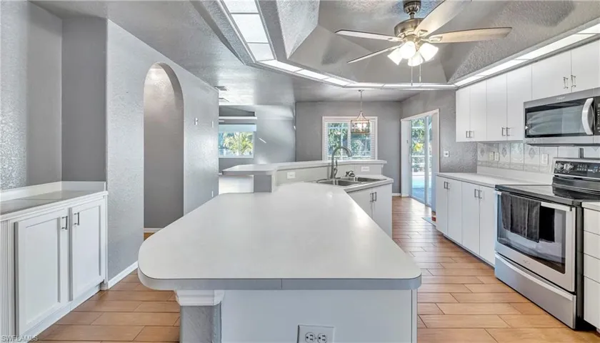 Kitchen with a textured wall, appliances with stainless steel finishes, white cabinets, a kitchen island with sink, and light countertops