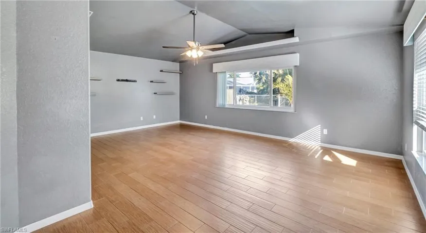 Spare room with a textured wall, light wood-style floors, a ceiling fan, and lofted ceiling
