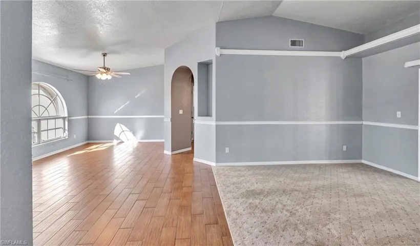 Unfurnished room featuring a textured ceiling, wood tiled floors, arched walkways, a ceiling fan, and vaulted ceiling