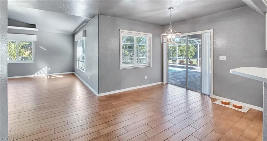 Unfurnished dining area with a textured wall, wood tiled floors, a textured ceiling, lofted ceiling, and a chandelier