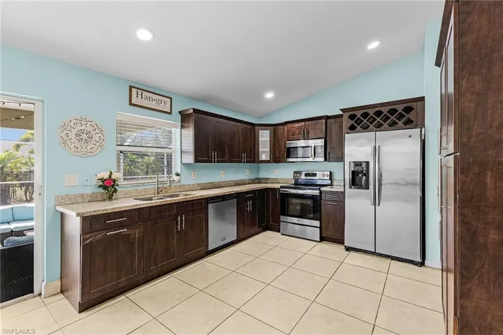 Kitchen featuring stainless steel appliances, a sink, dark brown cabinets, vaulted ceiling, and light tile patterned flooring