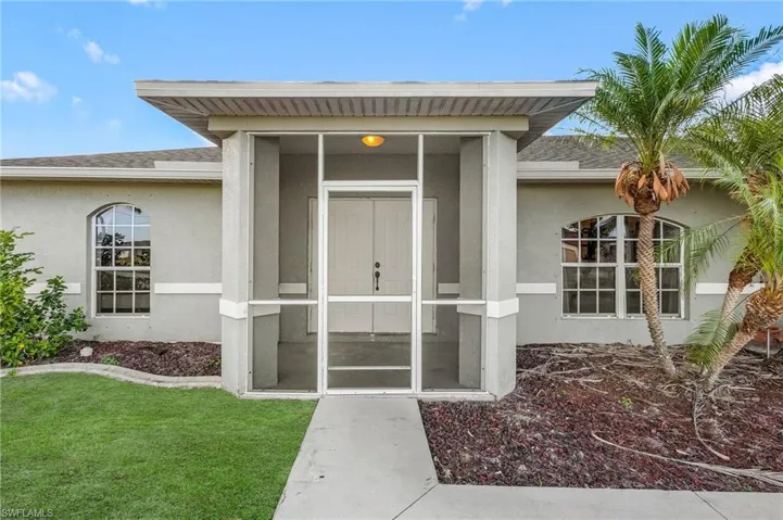 View of exterior entry featuring stucco siding, roof with shingles, and a yard