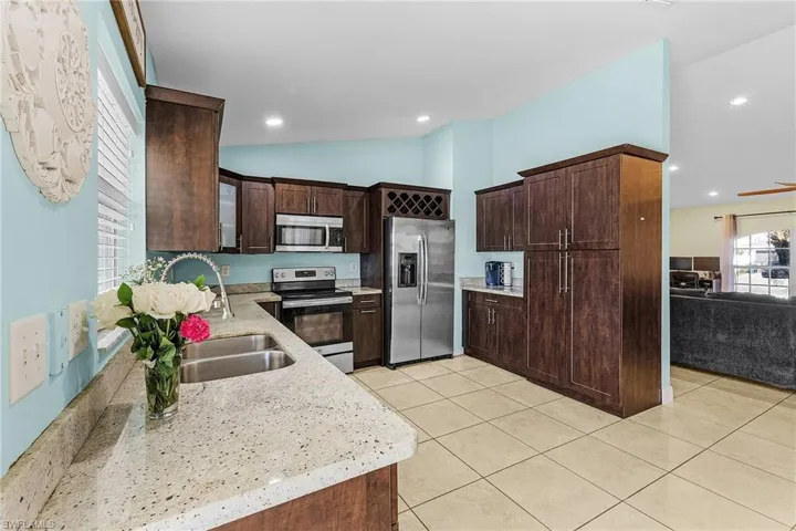 Kitchen with appliances with stainless steel finishes, dark brown cabinets, light tile patterned flooring, a sink, and lofted ceiling