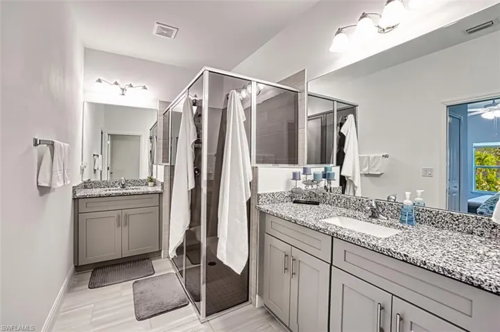 Bathroom featuring two vanities, ensuite bathroom, a stall shower, and a ceiling fan
