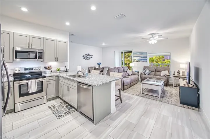 Kitchen featuring appliances with stainless steel finishes, a kitchen bar, a peninsula, light stone counters, and gray cabinets