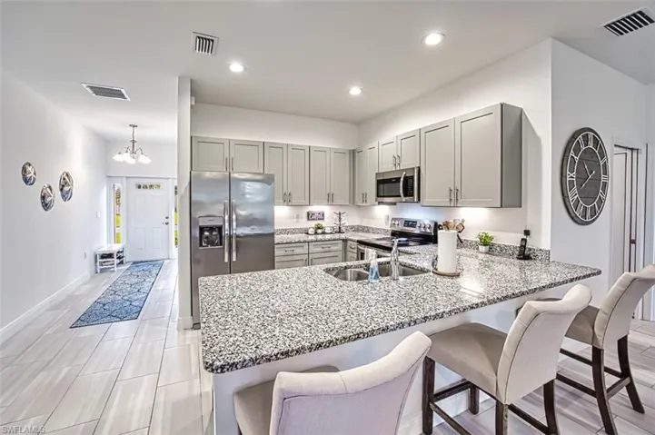 Kitchen featuring a kitchen breakfast bar, gray cabinets, stainless steel appliances, light stone countertops, and recessed lighting