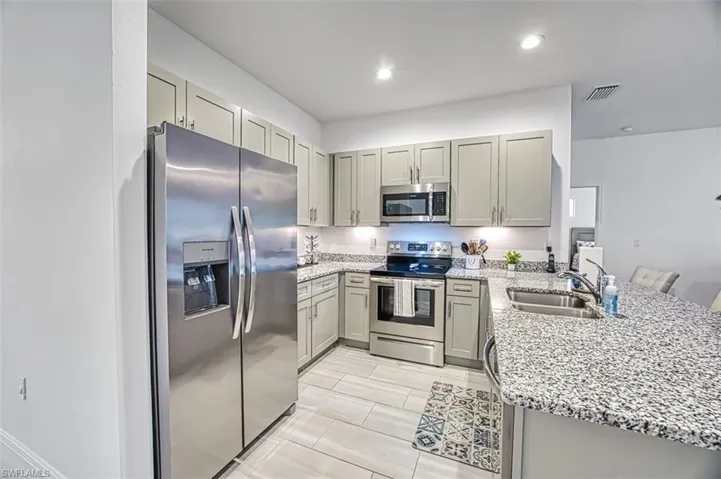 Kitchen featuring appliances with stainless steel finishes, a peninsula, gray cabinetry, light stone counters, and recessed lighting