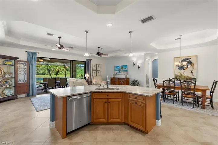 Kitchen with a tray ceiling, dishwasher, ceiling fan with notable chandelier, an island with sink, and hanging light fixtures
