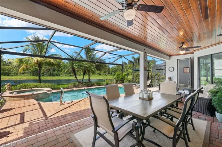 View of patio with glass enclosure, ceiling fan, and a pool with hot tub