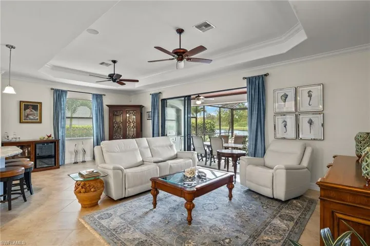 Living room with ornamental molding, ceiling fan, a raised ceiling, and plenty of natural light