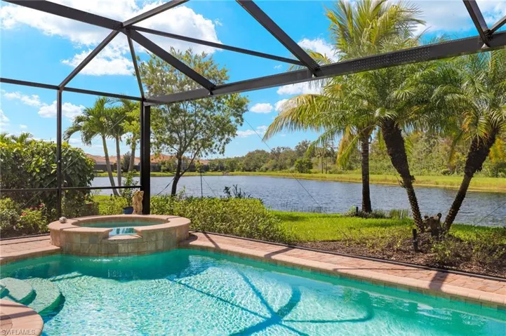 View of pool with glass enclosure, a water view, and an in ground hot tub
