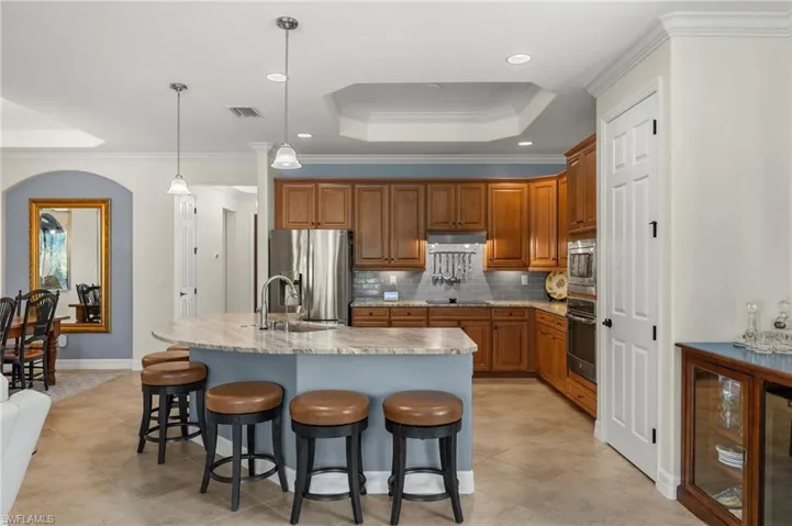 Kitchen with decorative light fixtures, a center island with sink, stainless steel appliances, a kitchen breakfast bar, and light stone countertops