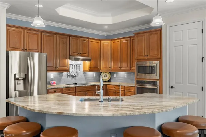 Kitchen featuring appliances with stainless steel finishes, a large island with sink, a breakfast bar area, decorative light fixtures, and sink