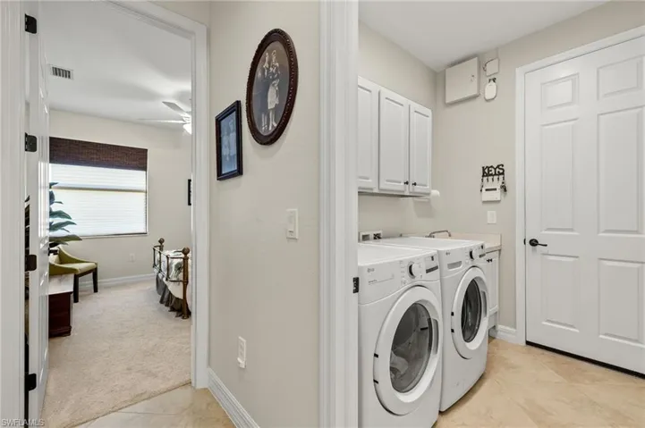 Clothes washing area with light tile patterned floors, independent washer and dryer, ceiling fan, and cabinets