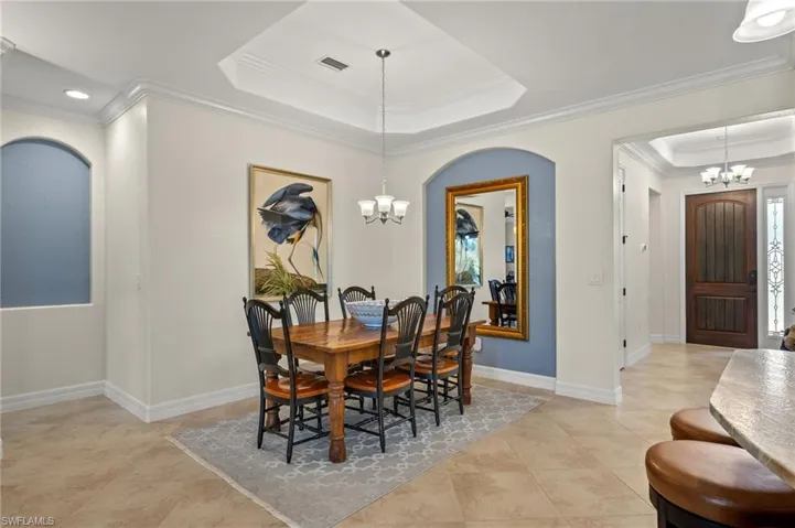 Dining area with a raised ceiling, crown molding, an inviting chandelier, and light tile patterned floors