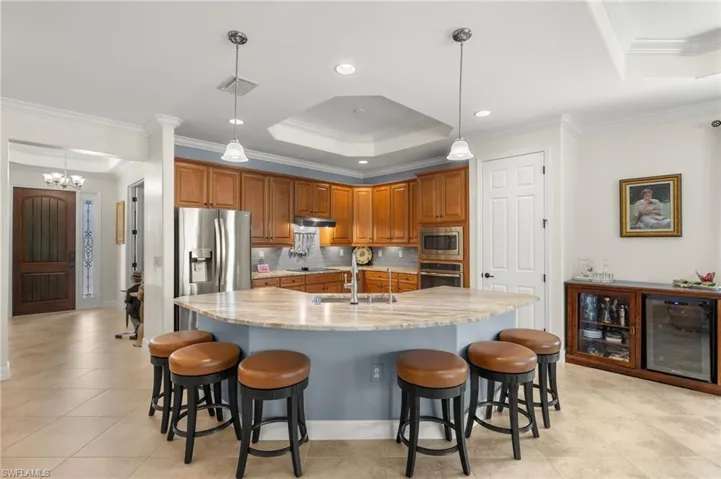 Kitchen featuring appliances with stainless steel finishes, crown molding, wine cooler, and hanging light fixtures