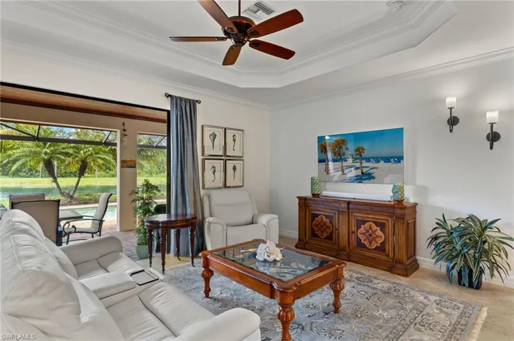 Tiled living room with a raised ceiling, ornamental molding, and ceiling fan