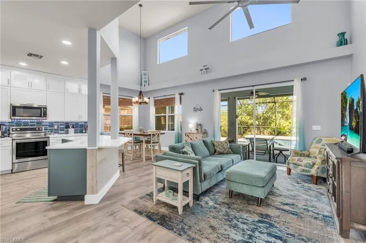 Living room featuring light hardwood / wood-style flooring, ceiling fan with notable chandelier, and high vaulted ceiling