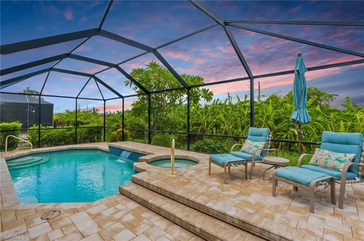 Pool at dusk featuring an in ground hot tub, glass enclosure, and a patio area