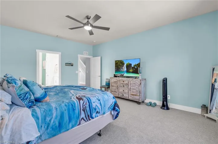 Bedroom with ceiling fan, connected bathroom, and light carpet