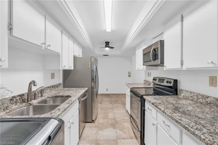 Kitchen with stainless steel appliances stainless steel appliances, a tray ceiling, ceiling fan, sink, and white cabinets
