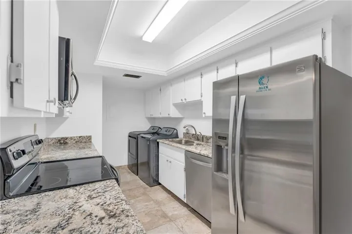 Kitchen featuring light stone countertops, stainless steel appliances, sink, separate washer and dryer, and white cabinets