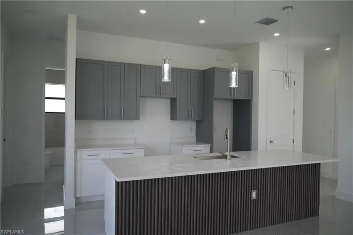 Kitchen with light stone countertops, gray cabinets, decorative light fixtures, a center island with sink, and recessed lighting