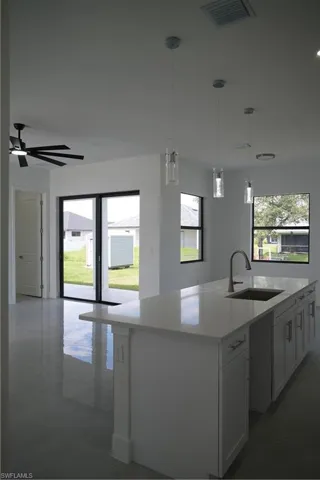 Kitchen featuring decorative light fixtures, open floor plan, an island with sink, light stone counters, and healthy amount of natural light