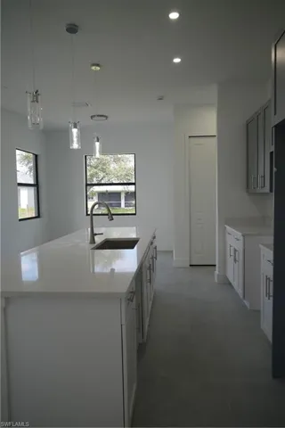 Kitchen with decorative light fixtures, recessed lighting, light stone countertops, a center island with sink, and gray cabinetry