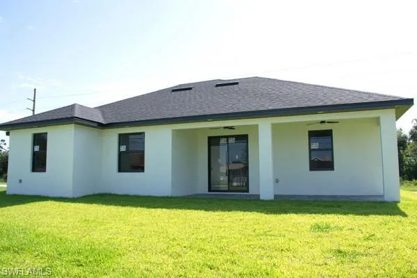 Rear view of property with ceiling fan and a lawn