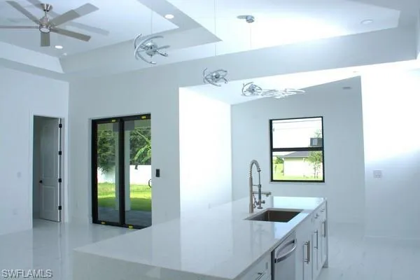 Kitchen with sink, white cabinetry, light stone counters, a tray ceiling, and decorative light fixtures