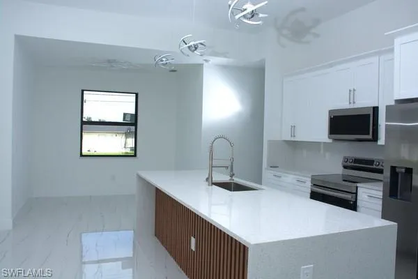 Kitchen with white cabinetry, sink, hanging light fixtures, a kitchen island with sink, and stainless steel appliances