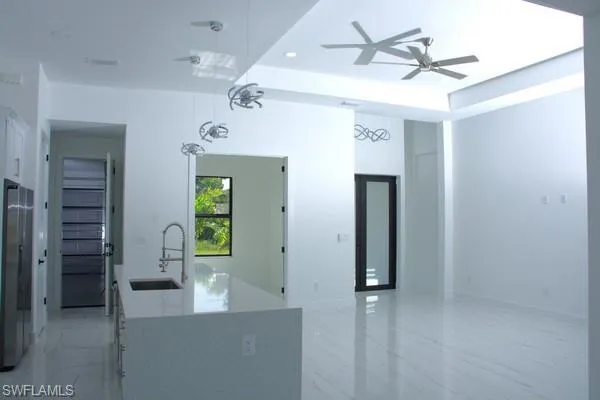 Kitchen with sink, ceiling fan, white cabinets, decorative light fixtures, and a raised ceiling