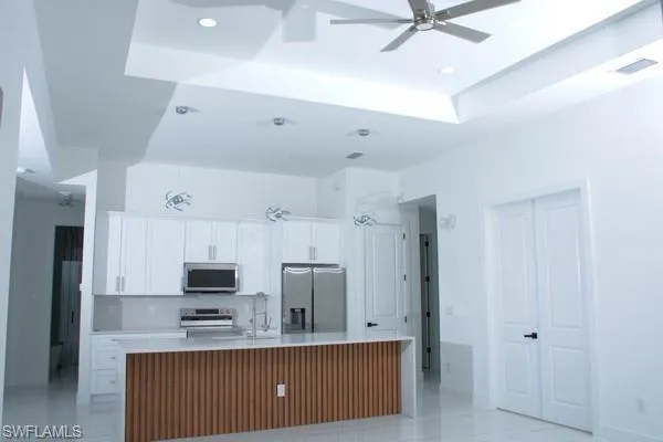 Kitchen featuring an island with sink, white cabinetry, backsplash, ceiling fan, and stainless steel appliances