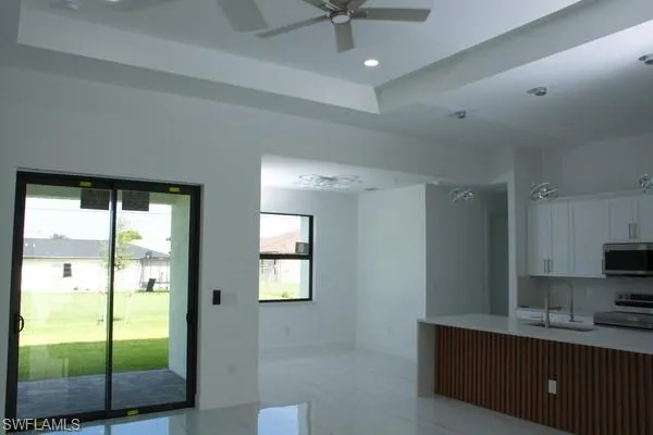 Kitchen featuring sink, a raised ceiling, ceiling fan, stainless steel appliances, and white cabinets