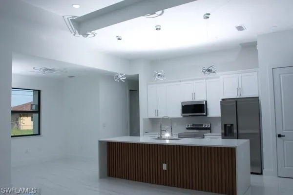 Kitchen with sink, a center island with sink, white cabinets, and appliances with stainless steel finishes