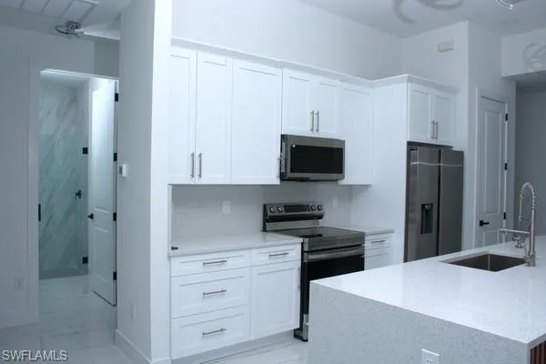 Kitchen featuring white cabinetry, an island with sink, sink, light stone counters, and stainless steel appliances