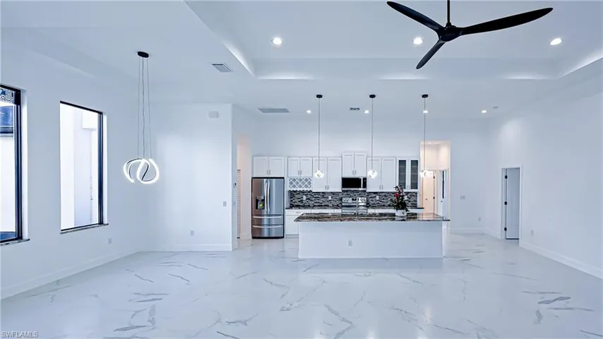 Kitchen with white cabinetry, open floor plan, stainless steel appliances, pendant lighting, and dark stone counters