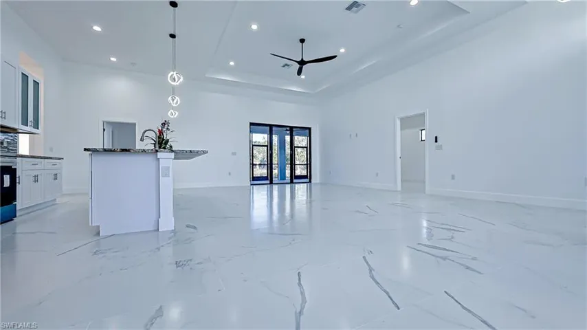 Kitchen featuring white cabinets, pendant lighting, an island with sink, open floor plan, and dark stone countertops