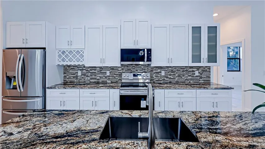 Kitchen featuring dark stone countertops, stainless steel appliances, white cabinetry, glass insert cabinets, and recessed lighting