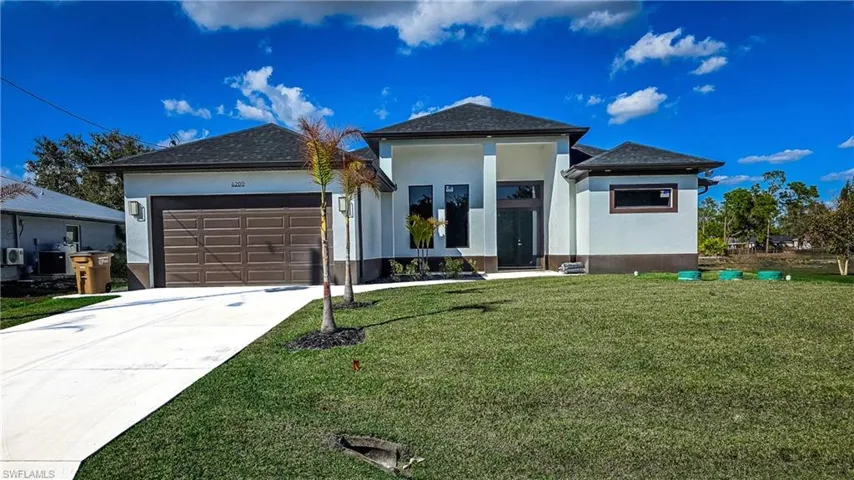 View of front of property featuring a garage, stucco siding, driveway, and a front yard
