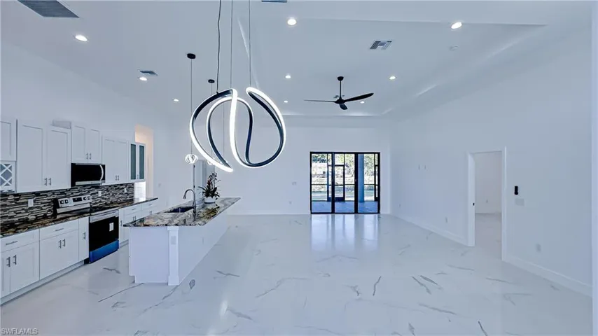 Kitchen with stainless steel appliances, white cabinetry, dark stone countertops, a center island with sink, and open floor plan