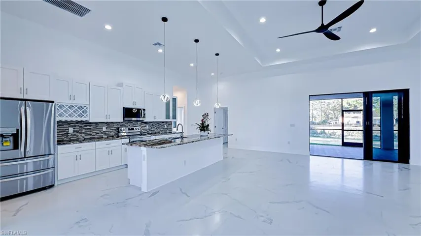 Kitchen featuring stainless steel appliances, open floor plan, white cabinetry, pendant lighting, and a center island with sink